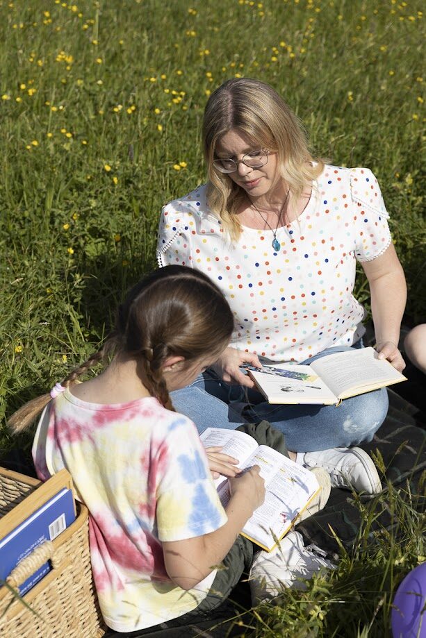 Ramona mit einem Mädchen und Büchern beim Üben in einer Blumenwiese